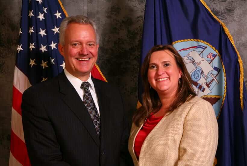 Jeannette King and a man standing in front of the West Virginia state flag and the American flag