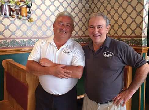 Brothers Al and Joe Leonoro stand smiling next to a booth in their restaurant