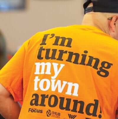 Man in a bright orange t-shirt that reads "I'm turning my town around" on the back