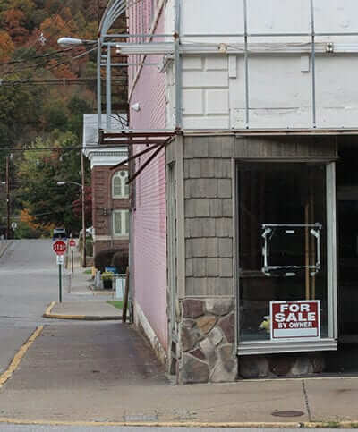 abandoned looking store with sign reading "for sale by owner"