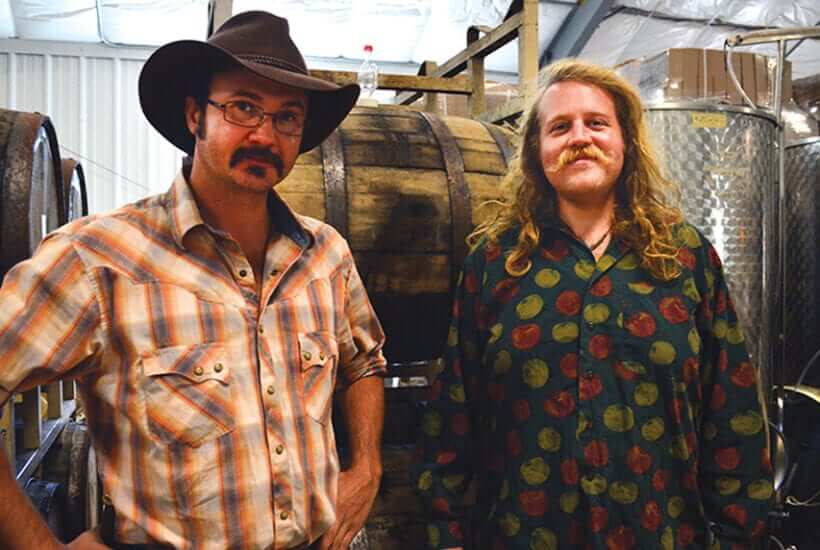 Josh Bennett and Well Lewis pose in front of their distillery.