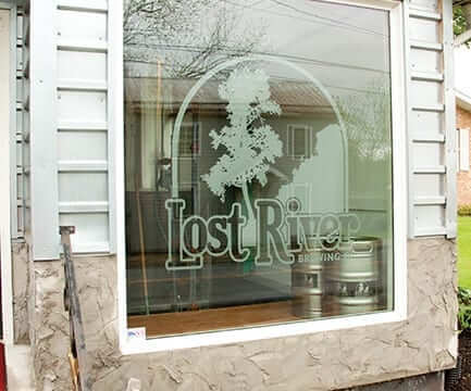 Frosted window that says "Lost River Brewing" with a tree illustration